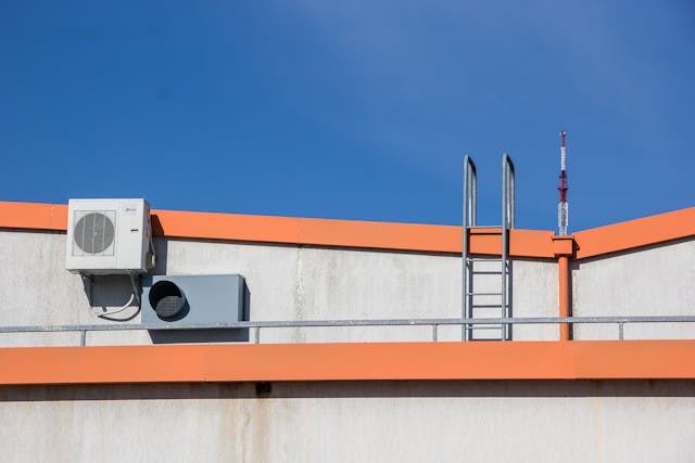 Air conditioning unit and ladder on a rooftop with orange trim under a clear blue sky